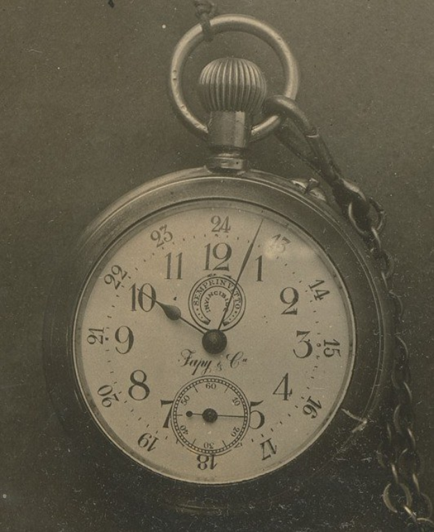 Ein Schwarz-Weiß-Foto einer antiken Taschenuhr mit einer Kette, mit einem nummerierten Zifferblatt.