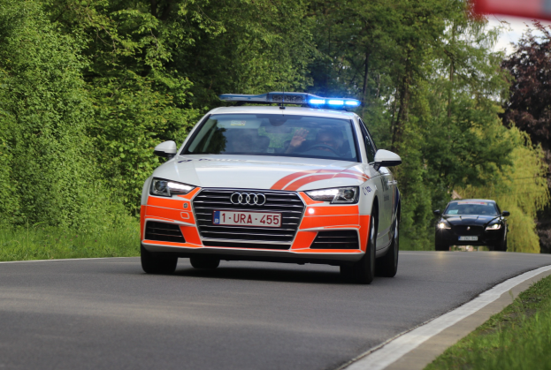 Ein Polizei-Audi A4 mit zwei Insassen fährt auf einer grasbewachsenen Straße neben einem Wald unter einem klaren blauen Himmel.