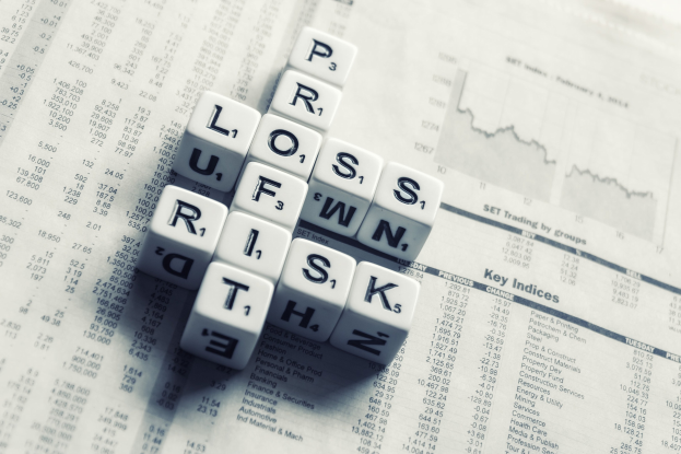 Kreuzworträtsel mit den Wörtern "Verlust", "Risiko" und "Risiko" auf einer Zeitung, die mit Finanztext und Zahlen gefüllt ist.
