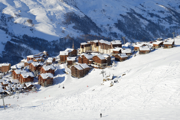 Ein Skigebiet in den französischen Alpen mit schneebedeckten Bergen, Gebäuden, Bäumen und Menschen, die die Pisten hinunterfahren.