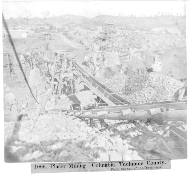 Schwarz-weiß-Foto eines Kohlebergwerks in Kolumbien mit Gebäuden, Bäumen und Bergen im Hintergrund sowie Text am unteren Rand.