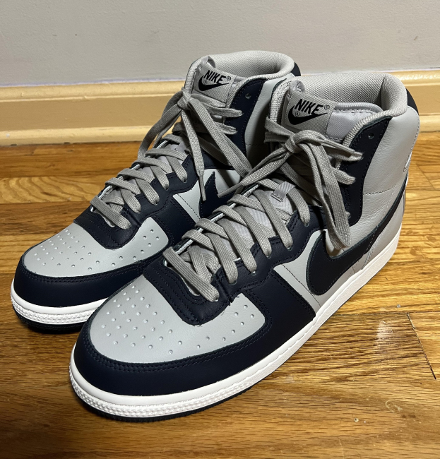 A pair of Nike Air Jordan 1 Retro High OG Midnight Navy shoes with white accents on a wooden floor, featuring the Nike swoosh logo on the side.