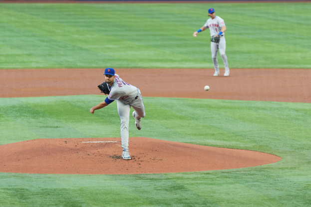 Baseballspieler in Uniform, der einen Ball auf einem Feld wirft, mit Zuschauern im Hintergrund.