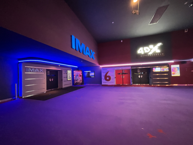 Innenseite eines Kinos mit lila Teppich, Text und Bildschirme an den Wänden und Deckenbeleuchtung.