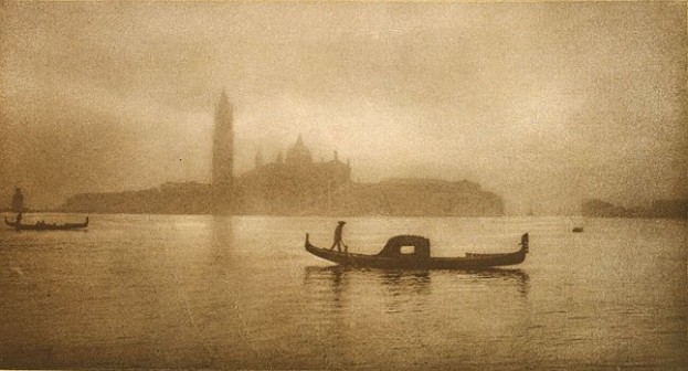 Schwarz-weiß-Foto einer Gondel in Venedig, Italien, mit einer Person darin, umgeben von anderen Booten und Gebäuden entlang der Wasserfront.