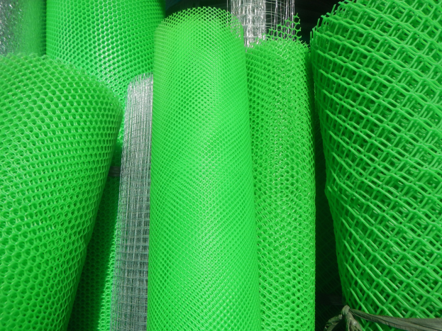 Green PVC coated welded wire mesh stacked in a dark warehouse, secured with rope.