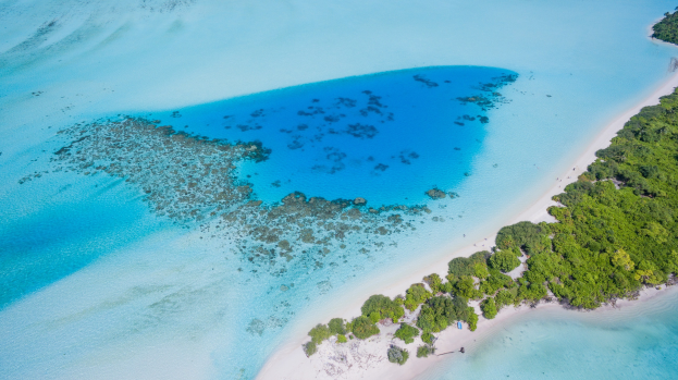 Aerial view of a small, lush green island surrounded by crystal clear blue ocean water.