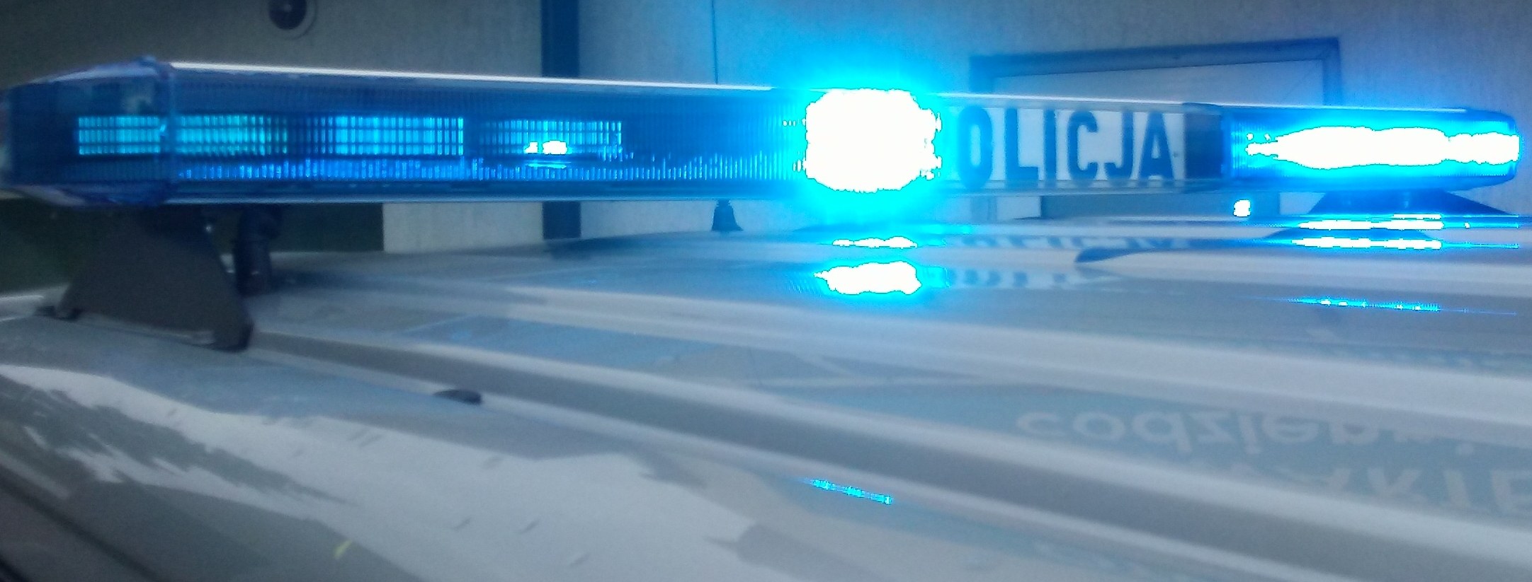 Polizeiauto mit blinkenden Lichtern an einer Wand geparkt.