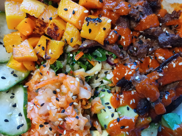 Nahaufnahme einer Schüssel mit bunten Gemüsen wie Karotten, Paprika, Zwiebeln und Pilzen auf Reis, garniert mit goldbraunem Fleisch.