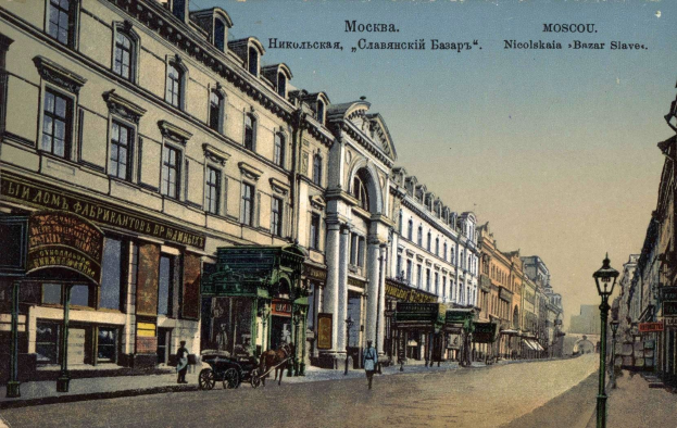 Schwarz-weiß-Postkarte einer Moskauer Straße mit Gebäuden, Straßenlaternen, Pferdefuhrwerken, Fußgängern und Schildern unter einem Himmel, mit Text oben.