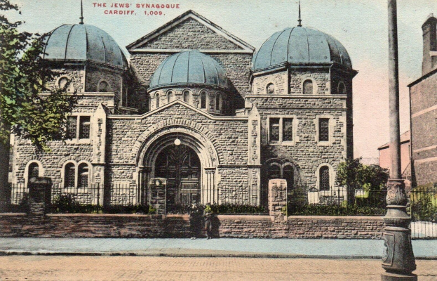 Alte Postkarte der jüdischen Synagoge in Cardiff, Ontario, Kanada, zeigt ein Gebäude mit Fenstern, Türen und Bögen, umgeben von Pflanzen, einem Zaun, Bäumen, einem Pfahl und einem bewölkten Himmel, mit Text oben.