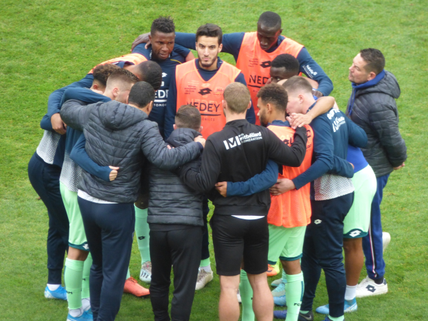 Eine Gruppe von Männern in Jacken, die sich auf einem Fußballfeld im Kreis versammeln.