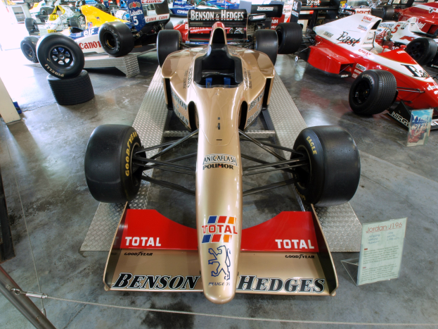 Rennwagen im Motorsportmuseum, durch einen Metallzaun von Besuchern im Hintergrund getrennt.