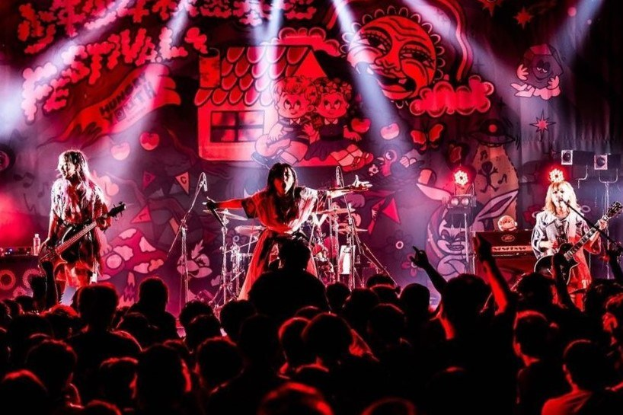 Ein Live-Auftritt der japanischen Rockband Korn auf der Bühne, mit Bandmitgliedern, die Gitarren spielen und in Mikrofone singen, während das Publikum unten zuschaut.