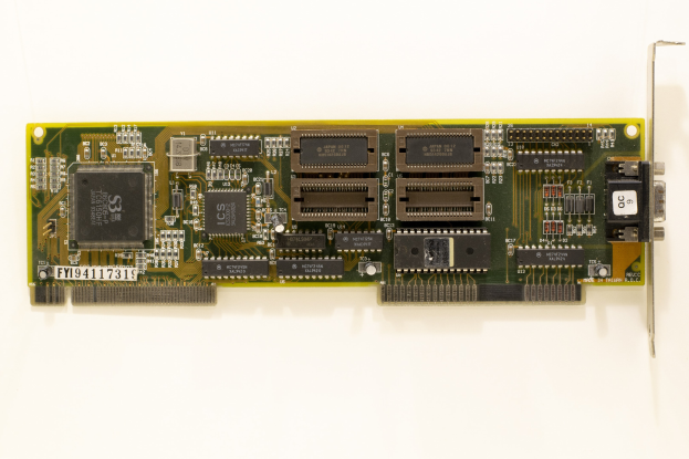 Nahaufnahme einer PCI-E-Karte mit einem zentralen Chip und mehreren angeschlossenen Verbindern auf einer weißen Oberfläche.