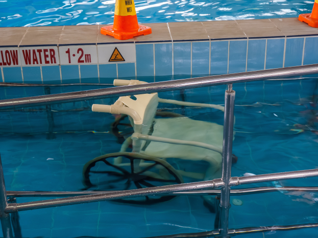 Schwimmbad mit einem Stuhl in der Mitte, umgeben von Sicherheitskonussen und einem Geländer und einem Schild an der Wand, das verfügbare Schwimmausrüstung anzeigt.