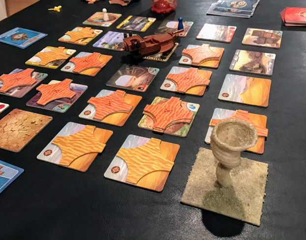 Ein unordentlicher Tisch mit Star Wars: The Old Republic Brettspiel-Karten, Spielzeugen und Gegenständen in einem Raum mit einer Wand im Hintergrund.