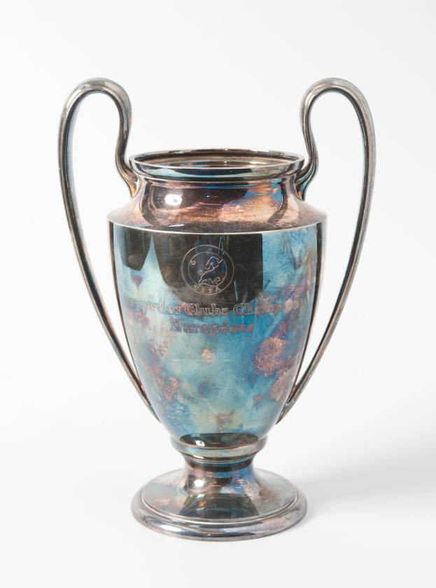 Der UEFA-Champions-League-Pokal, ein Stahlbecher mit zwei Griffen und einem blauen und silbernen Farbschema, der mit 'UEFA Champions League' beschriftet ist, vor einem weißen Hintergrund.