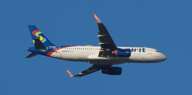 Spirit Airlines Airbus A320-200 im Flug mit weißer, blauer, roter und gelber Lackierung vor einem blauen Himmel.