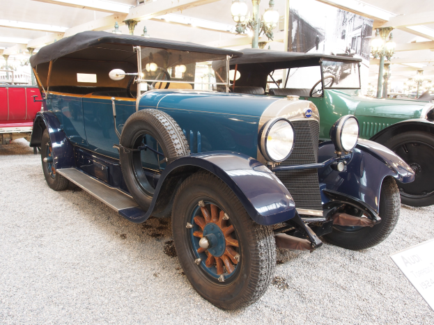 Ein vintage-blauer Wagen, der in einer Garage neben anderen Fahrzeugen geparkt ist, mit einer Tafel, auf der Text steht, rechts und an der Decke angebrachten Lampen.