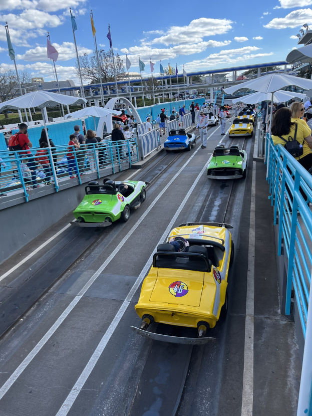 Menschen auf einer Achterbahn in Disney's Hollywood Studios, umgeben von Geländern, Fahnen, Bäumen und Gebäuden unter einem bewölktem Himmel.