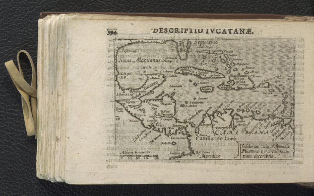 Offenes Buch mit einer detaillierten Karte der Karibik auf einer schwarzen Oberfläche, die Inseln und Gewässer zeigt.