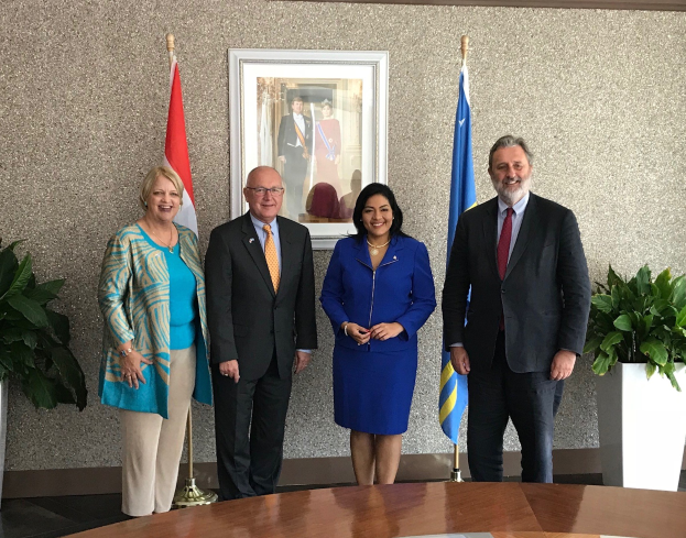 Eine Gruppe von Menschen, die um einen Tisch mit Papieren stehen und lächeln, umgeben von Fahnen, Topfpflanzen und einem Rahmenfoto an der Wand, was die Unterzeichnung eines U.S.-Canada Memorandum of Understanding anzeigt.