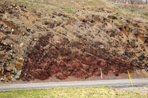 Ein großer Erdrutsch an der Seite einer Straße, mit Gras unten, einem Hügel in der Mitte und Bäumen und Himmel im Hintergrund.
