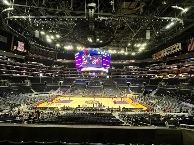 Eine große Halle, das Staples Center, voller Zuschauer bei einem Basketballspiel mit Sitzbereichen, Zuschauern, einem prominenten Bildschirm, einer Fahne, Anzeigetafeln und Deckenbeleuchtung.