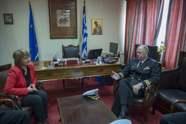 Zwei Personen, identifiziert als Stabschef und Staatssekretär, sitzen in Stühlen und sprechen in einem Raum mit einem Tisch in der Mitte, auf dem eine Mütze und ein Hut, Flaggen und Fotorahmen an der Wand, Vorhänge und ein Fenster auf der rechten Seite und ein weiterer Tisch mit einem Monitor, Tastatur, Maus, Telefon, Papieren, Büchern und anderen Gegenständen auf der linken Seite stehen.