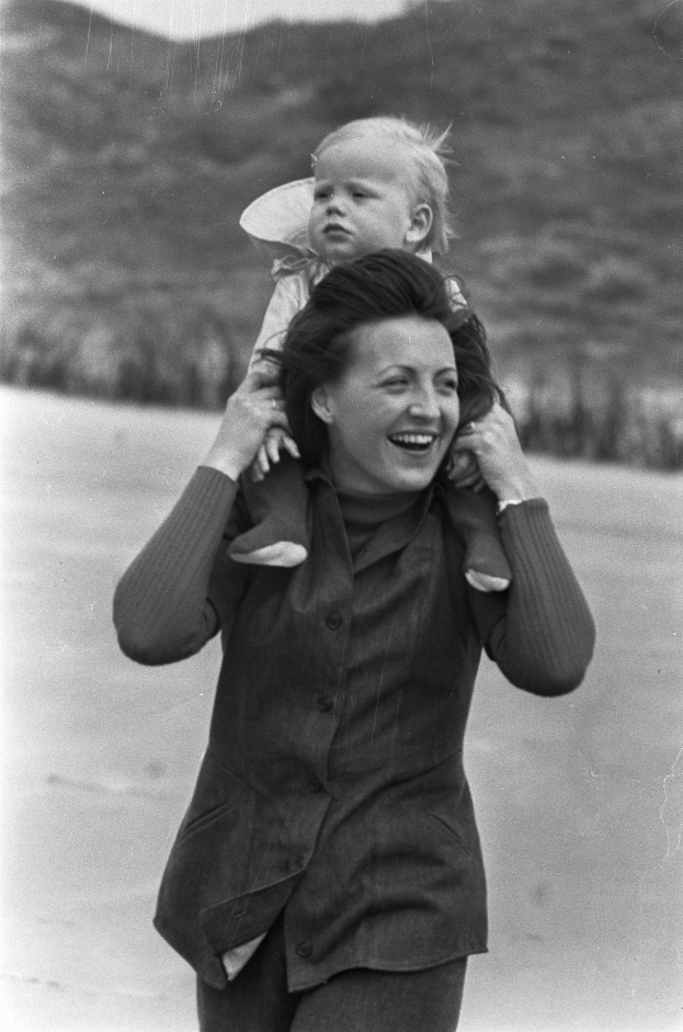 Eine Frau hält ein Baby in ihren Armen und strahlt ein warmes Lächeln, vor einem sanft unscharfen Hintergrund.