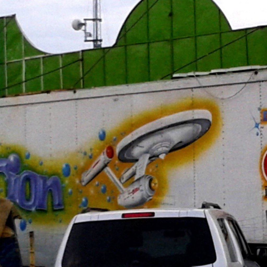 A car parked in front of a wall with a painting on it.