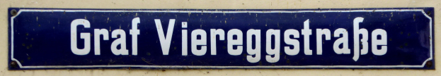 Blue and white rectangular sign on a building reading "Graf Viergeggstraße" in bold black lettering.