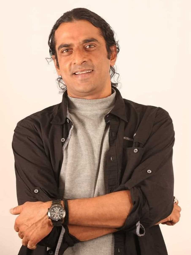 Ein Mann in einem schwarzen und aschgrauen Kleid steht mit verschränkten Armen vor einem weißen Hintergrund und trägt eine Uhr, während er tief nachdenkt.