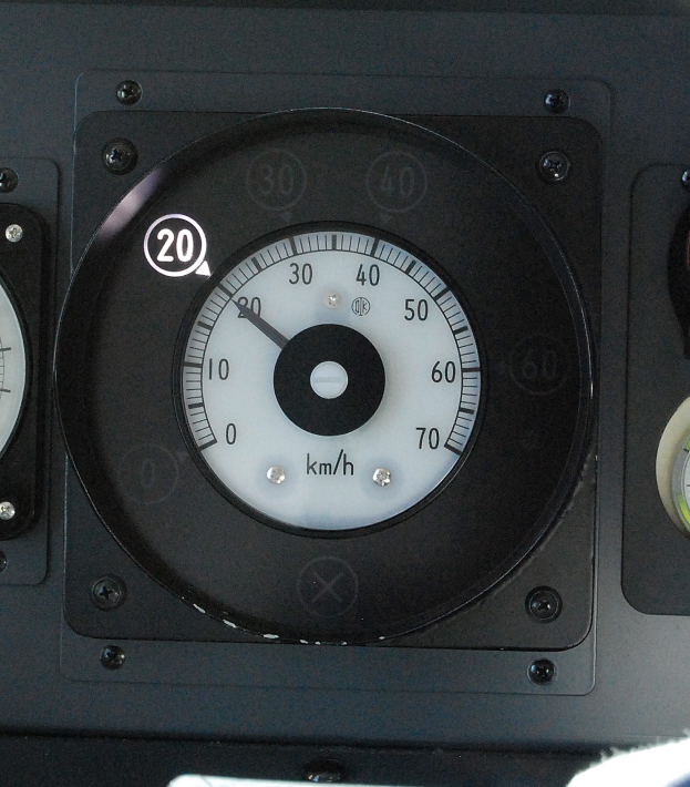 Close-up of an aircraft speedometer with a black face, white numbers, and a red needle indicating speed, flanked by two additional meters.