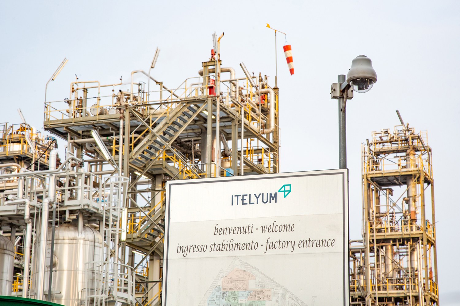 Ein großes industrielles Werk mit einem Schild davor, umgeben von Maschinen, Polen und Lichtern, unter einem klaren Himmel, Teil der italienischen Öl- und Gasindustrie.