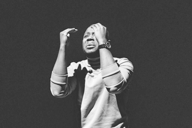 Ein Mann in einem T-Shirt und einer Uhr steht mit den Händen auf dem Kopf vor einem schwarzen Hintergrund und sieht besorgt aus, wahrscheinlich wegen einer Festnahme wegen Raub.