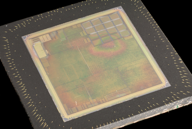 Nahaufnahme eines rechteckigen Halbleiterchips mit metallischem Glanz, dünnem Metallrahmen und kleinen Löchern an seinen Kanten, vor schwarzem Hintergrund.