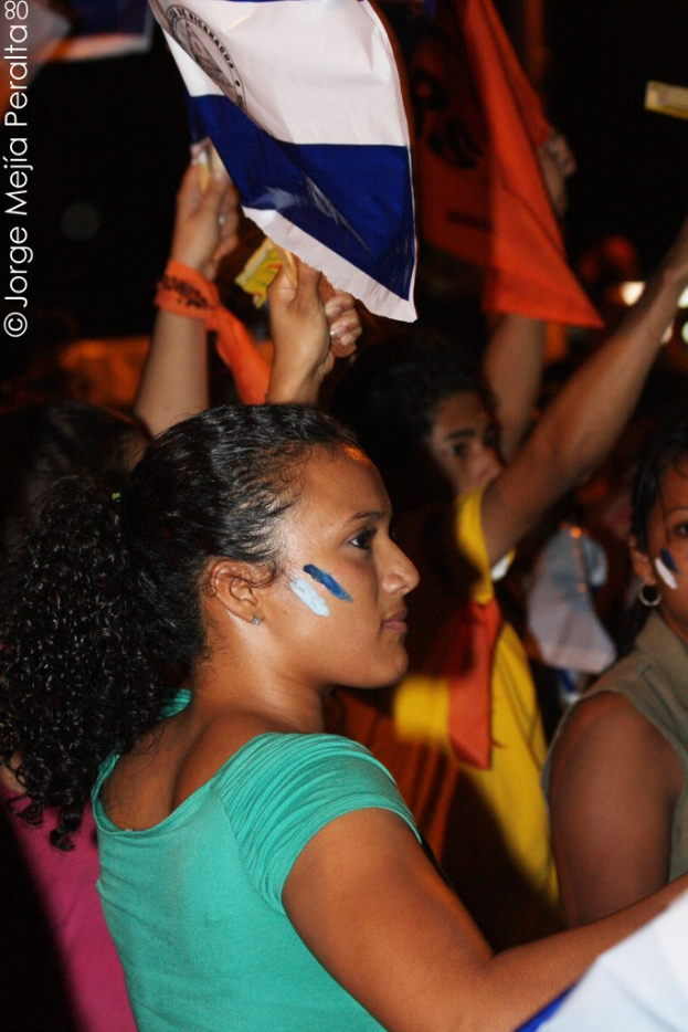 Frauen in grünen T-Shirts bei einer Demonstration, die weiße Stoffe halten, mit mehreren Mädchen im Hintergrund.
