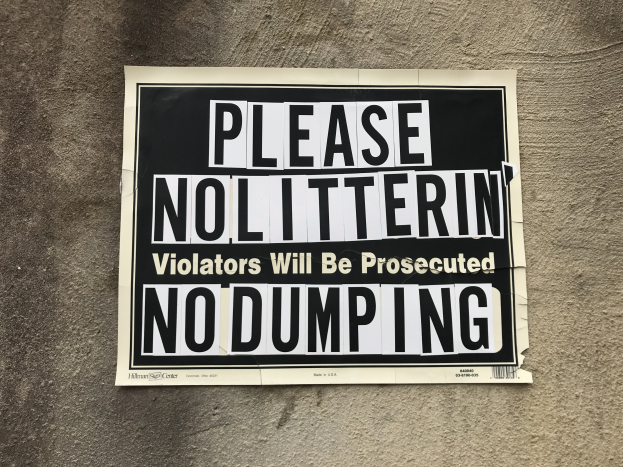Schwarzes und weißes Schild auf einem Gebäude mit der Aufschrift "Bitte keine Verschmutzung, Verursacher werden verfolgt - Keine Ablagerung."