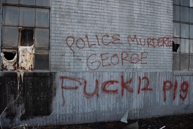 Graffiti an einer Gebäudewand mit der Aufschrift "Polizei Mord George Fuck 12 P19" und Fenstern und verstreuten Gegenständen davor.