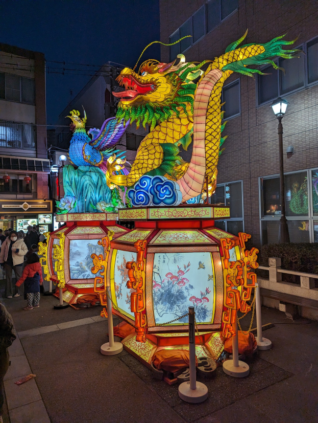A vibrant Chinese lantern festival in San Francisco with people admiring intricate lantern designs against a deep blue sky and illuminated buildings.