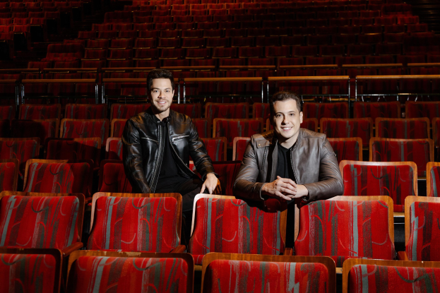 Zwei Männer in schwarzen Jacken, die während einer *Dancing with the Stars*-Vorstellung in roten Auditoriumsstühlen lächeln.