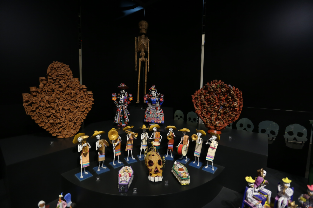 Vitrine mit verschiedenen Spielzeugen, darunter Puppen, Schädel und andere Gegenstände vor dunklem Hintergrund.