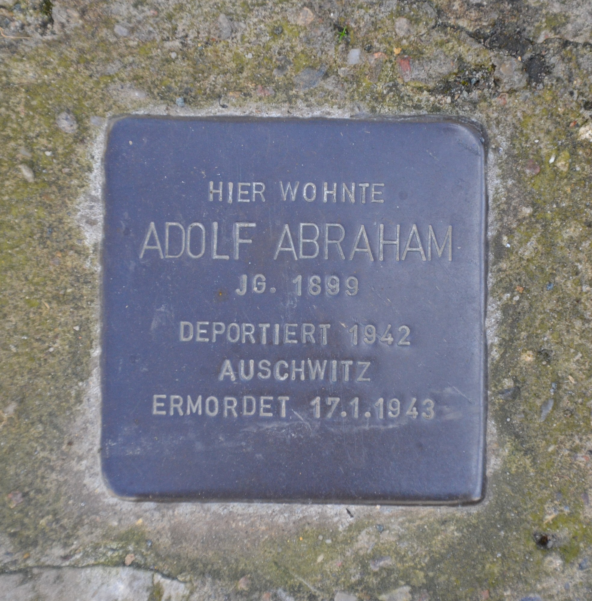 Rechteckige Plakette mit eingravierter Inschrift "Adolf Abraham" auf einer Steinwand montiert.