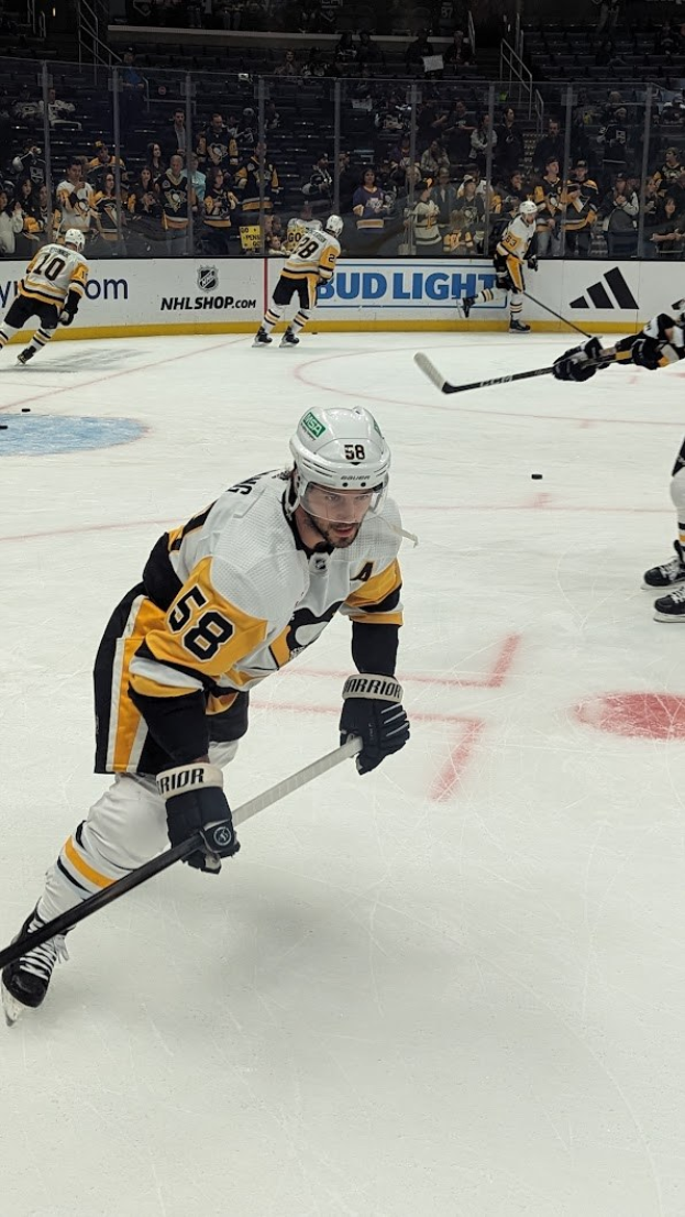 Gruppe von Menschen, die Hockey auf einem Eisplatz spielen, tragen Sportbekleidung, Helme und Turnschuhe und halten jeweils einen Hockeystock, mit Brettern, Geländern und Stufen im Hintergrund.