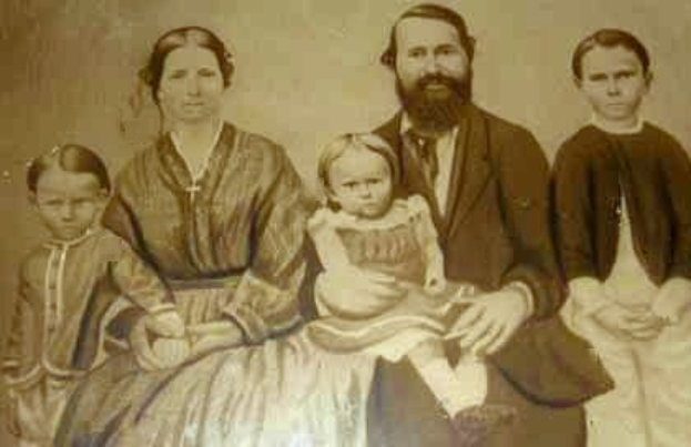 Ein Schwarz-Weiß-Foto einer Familie, die zusammen posiert, wobei ein Mann ein Baby in der Mitte hält und andere drumherum stehen.