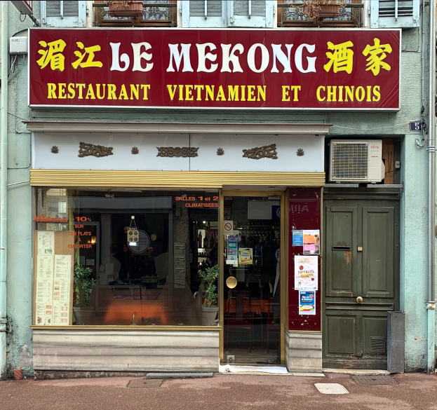 Außenansicht des Le Mekong Restaurants mit einem Schild, das "Le Mekong Restaurant Vietnam et Chinois" zeigt, einer Glastür mit Papieren, Topfpflanzen, Deckenleuchten, Rohren, Fenstern, einer Tür und einem Weg.