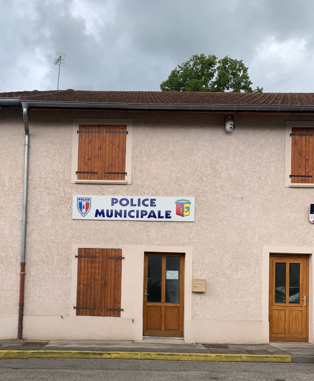 Polizei-Gebäude mit einem Schild, Fenstern, Türen, einer Namensplakette, einem Rohr, einem Baum und einem bewölkten Himmel im Hintergrund.