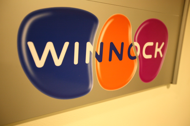 Hell leuchtendes "Winnock"-Schild an einer Wand, das einen Aktienmarkt anzeigt.